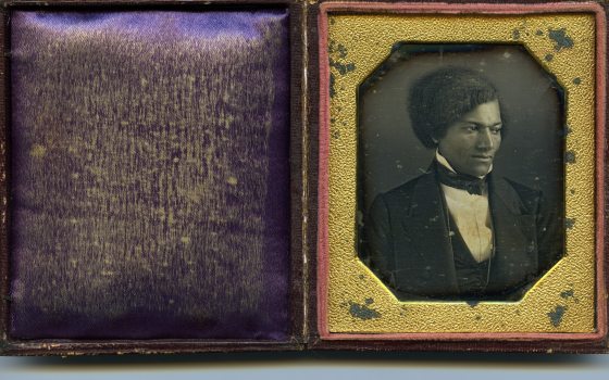 An old frame containing a black and white image of a person in a tuxedo, surrounded by a gold inset on the frame.